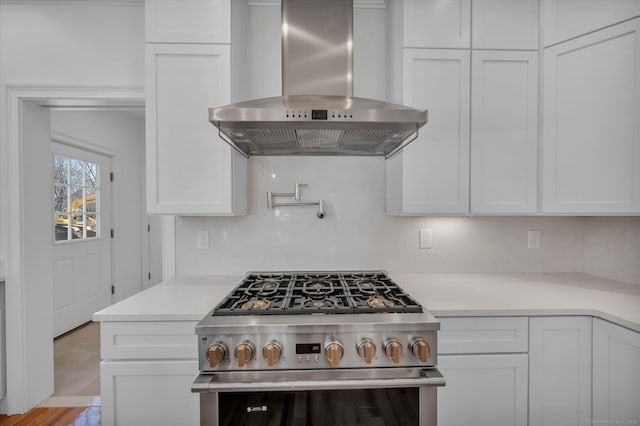 kitchen with stainless steel gas range, light countertops, wall chimney range hood, and white cabinetry