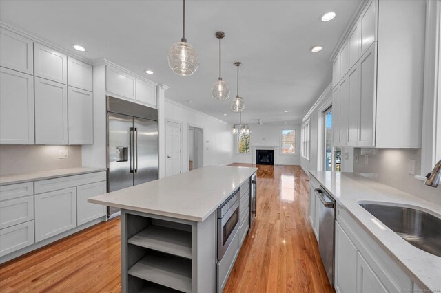 kitchen with built in appliances, hanging light fixtures, a sink, and white cabinetry