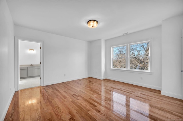 unfurnished bedroom featuring light wood-style floors, visible vents, baseboards, and ensuite bathroom