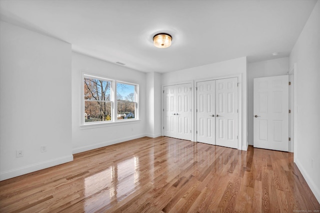 unfurnished bedroom with light wood-type flooring, visible vents, baseboards, and two closets