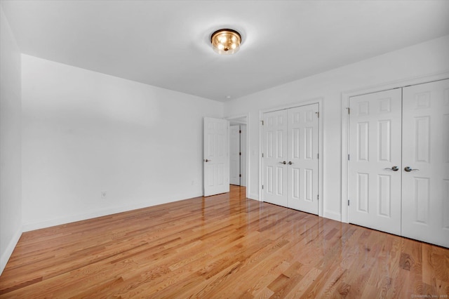 unfurnished bedroom featuring light wood-style floors, baseboards, and two closets