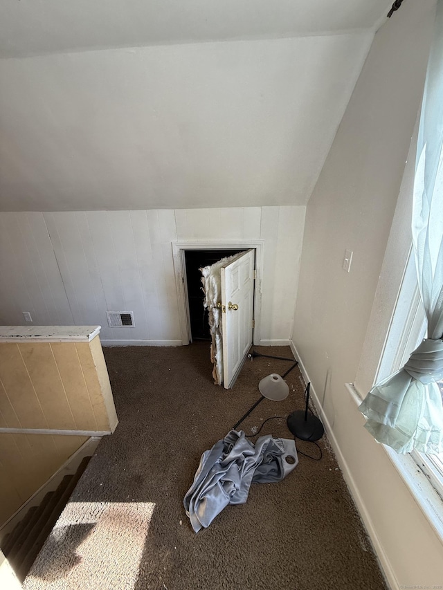 additional living space with visible vents, dark colored carpet, baseboards, and vaulted ceiling