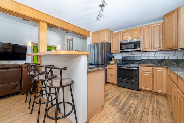 kitchen featuring tasteful backsplash, appliances with stainless steel finishes, a breakfast bar, and light wood-style floors