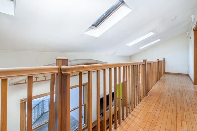 corridor with lofted ceiling with skylight and light wood-style flooring