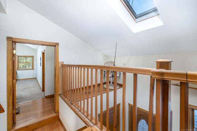 hallway featuring vaulted ceiling with skylight, baseboards, wood finished floors, and an upstairs landing