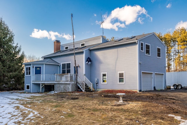 rear view of house featuring an attached garage, a chimney, and a wooden deck