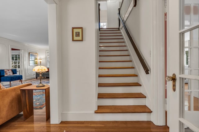 stairway with wood finished floors and ornamental molding