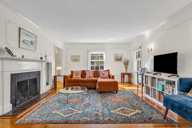 living area with wood finished floors, a brick fireplace, and ornamental molding