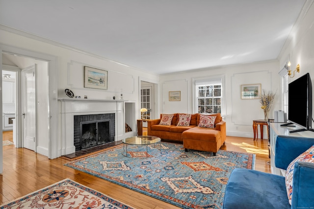 living room featuring crown molding, light wood-style flooring, a fireplace, and baseboards