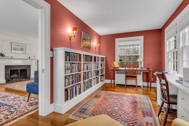 office area featuring baseboards, radiator, a brick fireplace, and wood finished floors