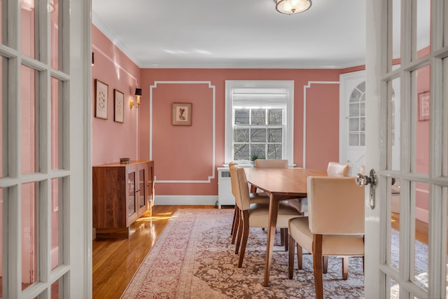 dining space with radiator, wood finished floors, baseboards, and ornamental molding