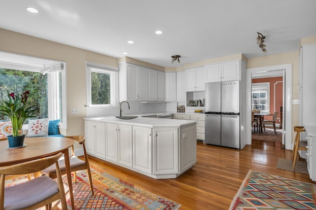 kitchen with light countertops, a peninsula, freestanding refrigerator, light wood-style floors, and a sink