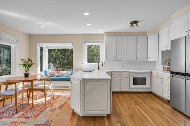 kitchen with electric range, freestanding refrigerator, decorative backsplash, light countertops, and light wood-style floors