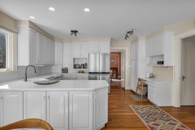 kitchen featuring a sink, wood finished floors, built in desk, freestanding refrigerator, and light countertops