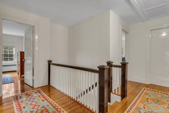 hallway with light wood-style floors, an upstairs landing, radiator, and baseboards