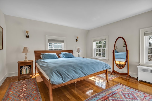 bedroom with multiple windows, radiator heating unit, baseboards, and wood-type flooring