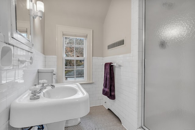 full bath featuring tile patterned flooring, a wainscoted wall, a stall shower, tile walls, and a sink