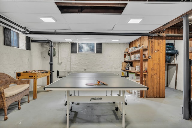 recreation room with a drop ceiling, concrete floors, and a textured wall