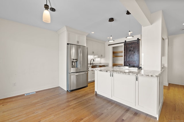 kitchen featuring a barn door, a sink, white cabinetry, light stone countertops, and stainless steel fridge