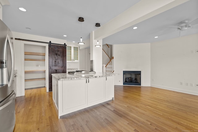 kitchen with a barn door, white cabinets, stainless steel refrigerator with ice dispenser, light stone countertops, and pendant lighting