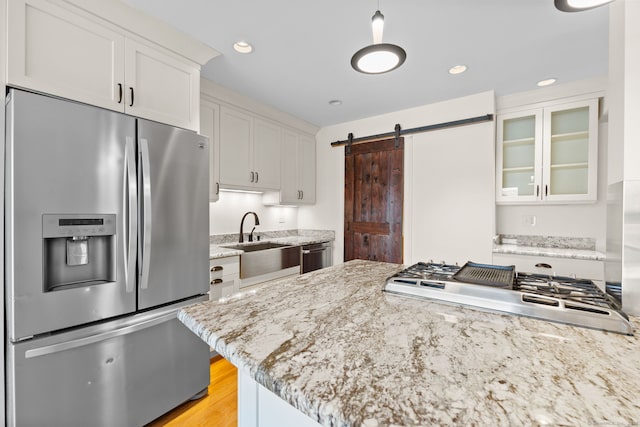 kitchen featuring appliances with stainless steel finishes, a barn door, glass insert cabinets, and white cabinetry