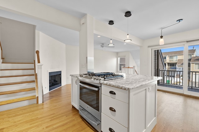 kitchen featuring a fireplace, white cabinets, stainless steel range with gas cooktop, light wood finished floors, and decorative light fixtures