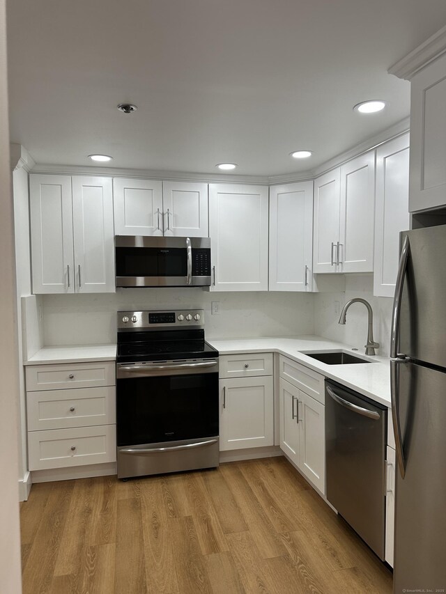 kitchen with a sink, light countertops, white cabinets, appliances with stainless steel finishes, and light wood-type flooring