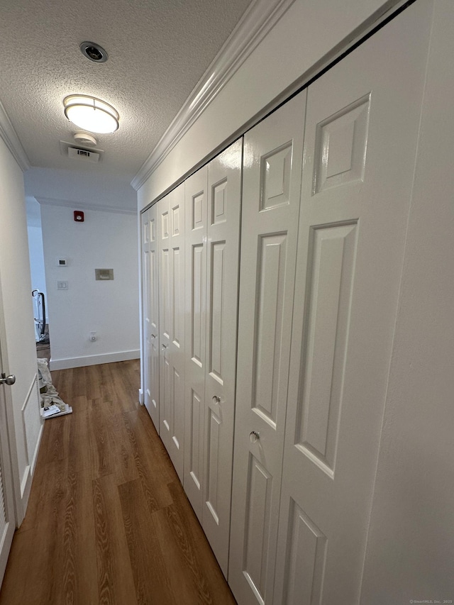 hallway with visible vents, crown molding, baseboards, wood finished floors, and a textured ceiling