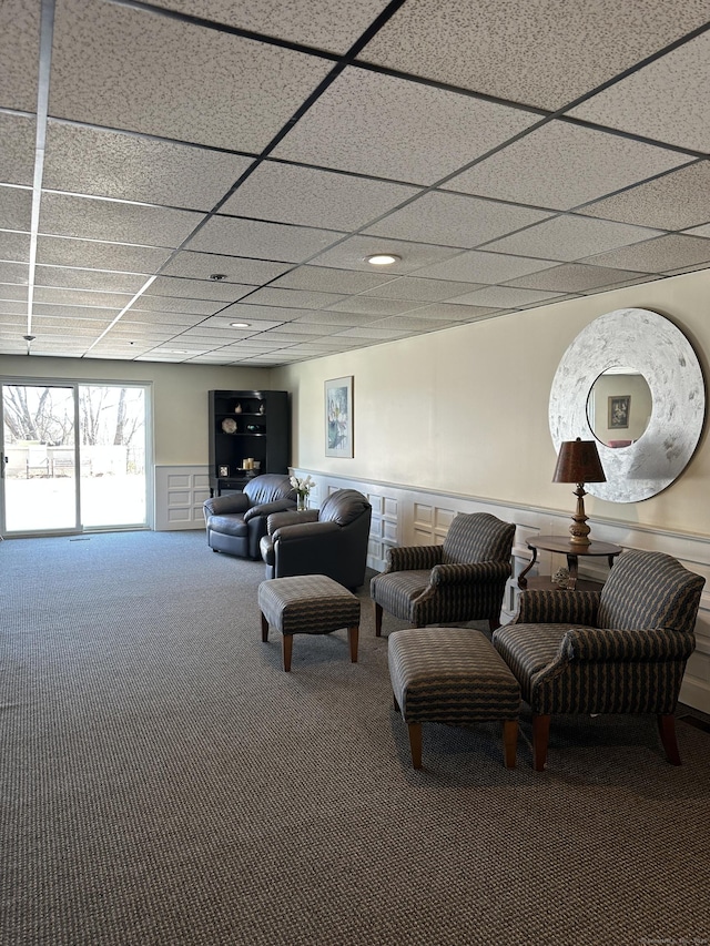 living area with a drop ceiling, a wainscoted wall, and carpet flooring