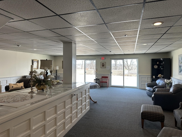 carpeted living room with a drop ceiling and a wainscoted wall