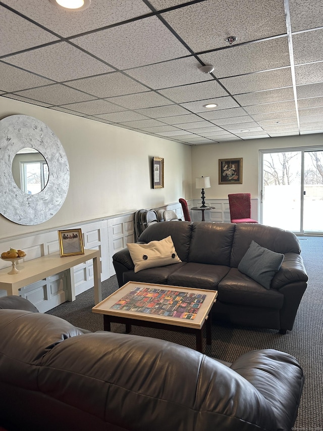 living area with a decorative wall, wainscoting, a paneled ceiling, and carpet