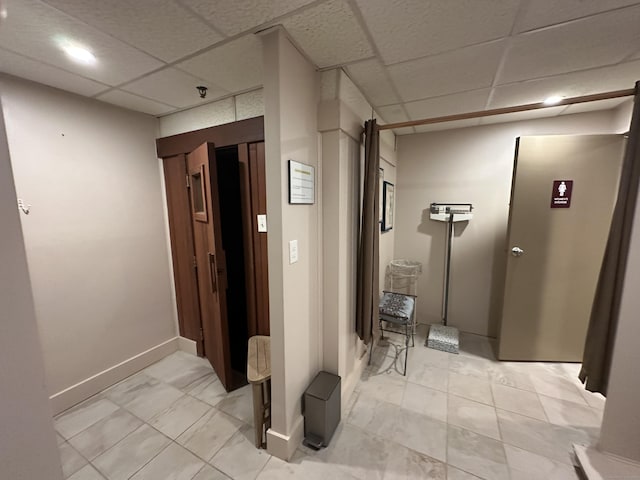 corridor featuring a drop ceiling and baseboards