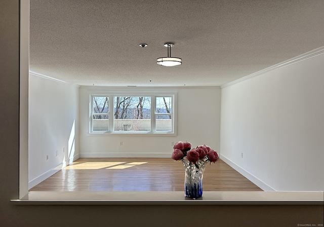 unfurnished dining area with baseboards, wood finished floors, a textured ceiling, and ornamental molding