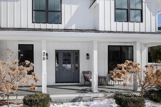 view of exterior entry featuring covered porch, board and batten siding, and roof with shingles