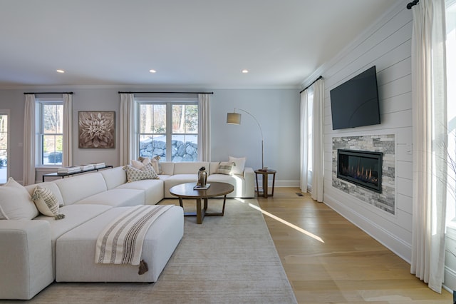 living area with crown molding, recessed lighting, light wood-style flooring, a glass covered fireplace, and baseboards