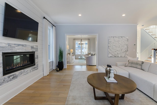 living area with stairs, light wood-type flooring, a glass covered fireplace, and crown molding