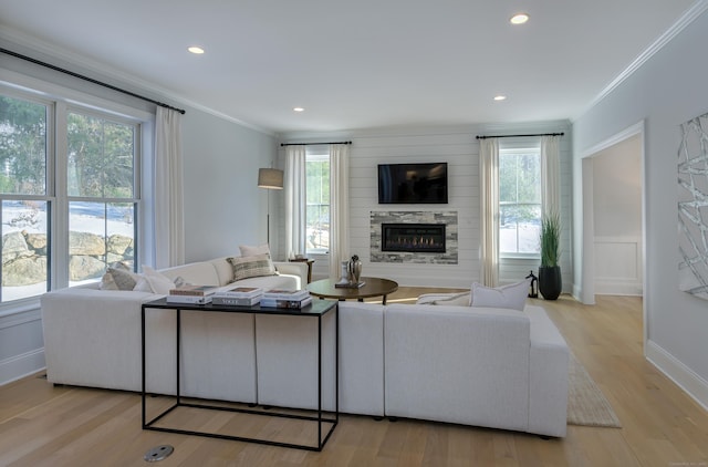 living area with a glass covered fireplace, crown molding, light wood finished floors, and recessed lighting