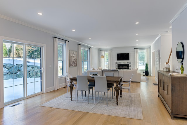 dining space featuring visible vents, ornamental molding, a fireplace, and light wood-style flooring