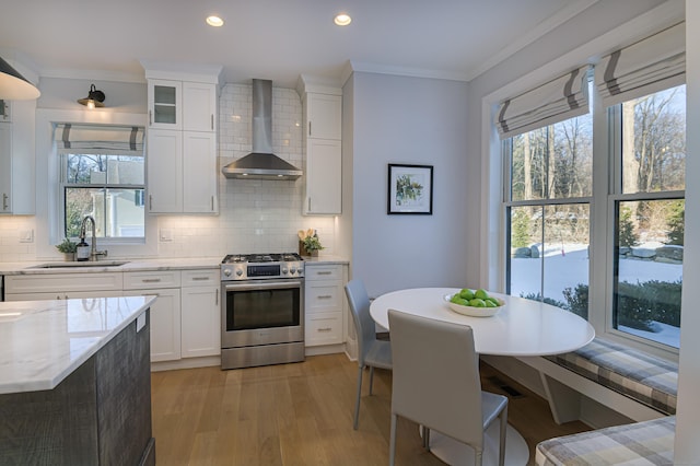 kitchen with wall chimney exhaust hood, glass insert cabinets, white cabinetry, a sink, and gas stove