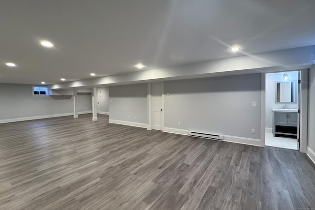 finished below grade area featuring dark wood-type flooring, a baseboard radiator, a sink, and baseboards