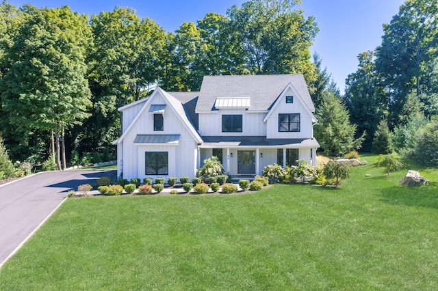 modern inspired farmhouse featuring aphalt driveway, a front yard, covered porch, and a shingled roof