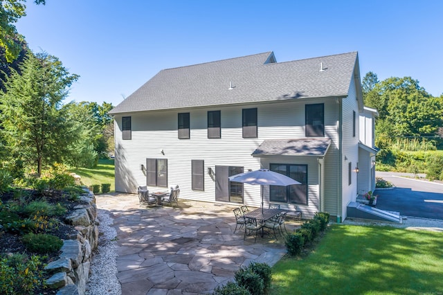 rear view of property featuring a shingled roof, a patio, and a lawn