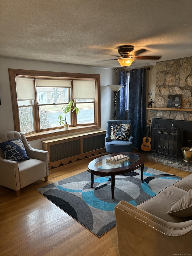 living area with a textured ceiling, a stone fireplace, radiator heating unit, and wood finished floors