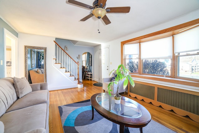 living room featuring baseboards, arched walkways, ceiling fan, stairway, and wood finished floors