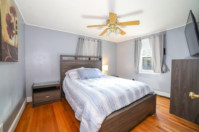 bedroom featuring baseboards, a baseboard heating unit, crown molding, a ceiling fan, and wood finished floors