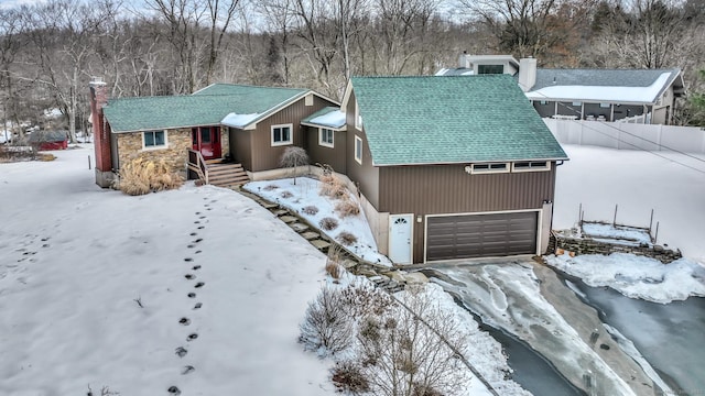 chalet / cabin with stone siding, roof with shingles, a chimney, and an attached garage