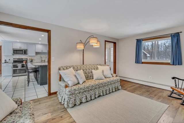 living room with light wood finished floors, a baseboard radiator, baseboards, and recessed lighting