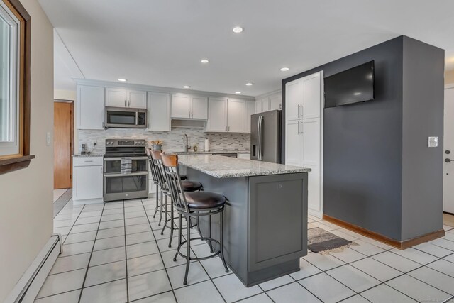 kitchen with a center island, stainless steel appliances, baseboard heating, white cabinetry, and light stone countertops