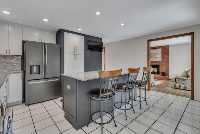 kitchen featuring light stone countertops, light tile patterned floors, stainless steel fridge, and white cabinetry