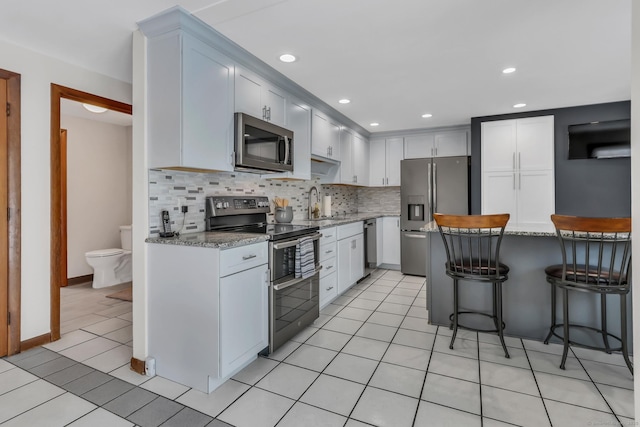 kitchen with tasteful backsplash, appliances with stainless steel finishes, light stone counters, and white cabinets